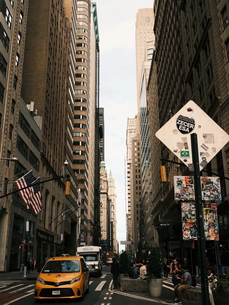 Broadway in the Financial District, a yellow cab under a road sign covered in stickers